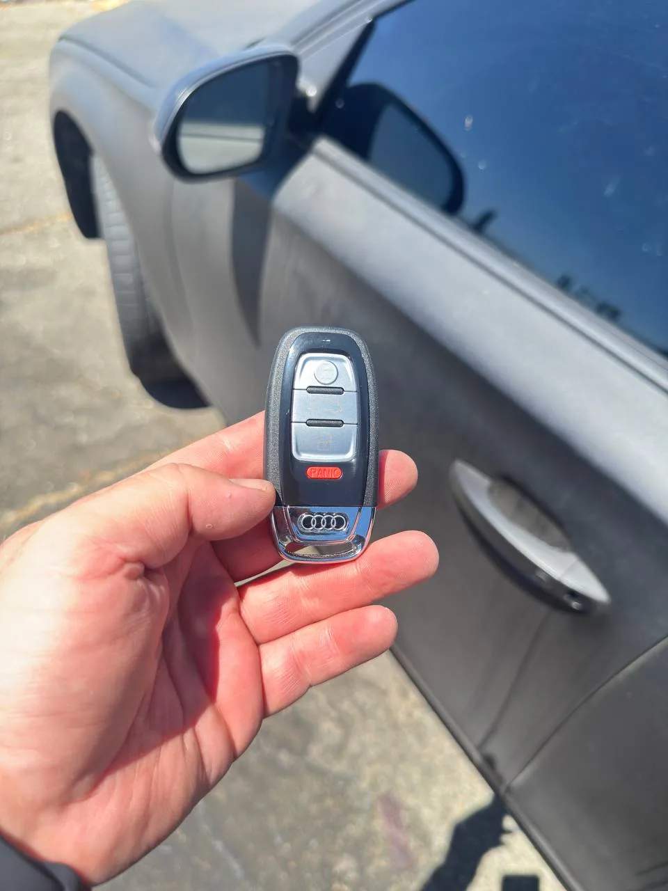 Freshly duplicated BMW key fob held beside the driver door of the vehicle