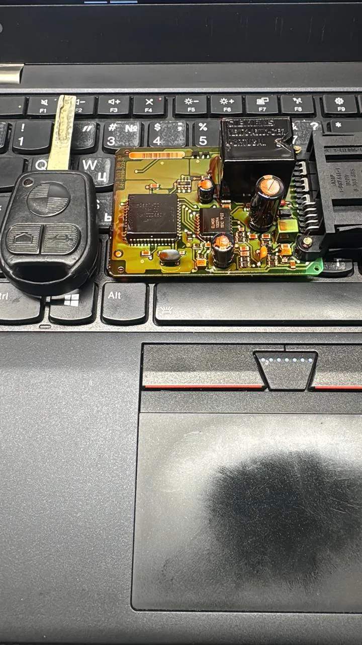 Locksmith holding a BMW key and circuit board on a laptop keyboard during bench key work