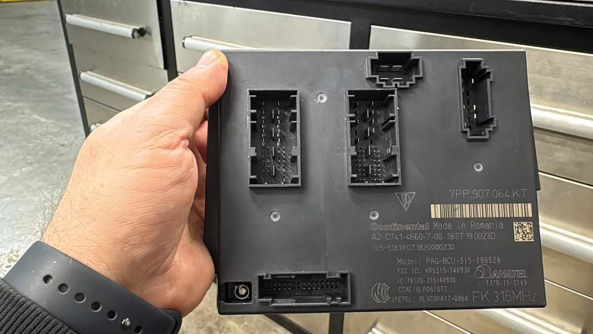 Body control module held in hand on a workshop bench during programming work