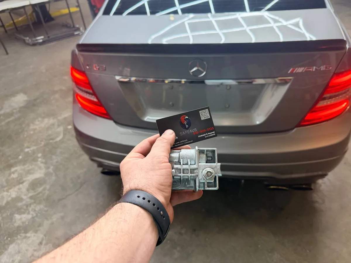 Safe4us technician holding a Mercedes-Benz ignition lock module and business card behind the vehicle