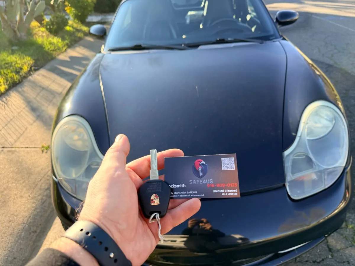 Locksmith holding a Porsche key and Safe4us business card in front of a Porsche during an all-keys-lost job