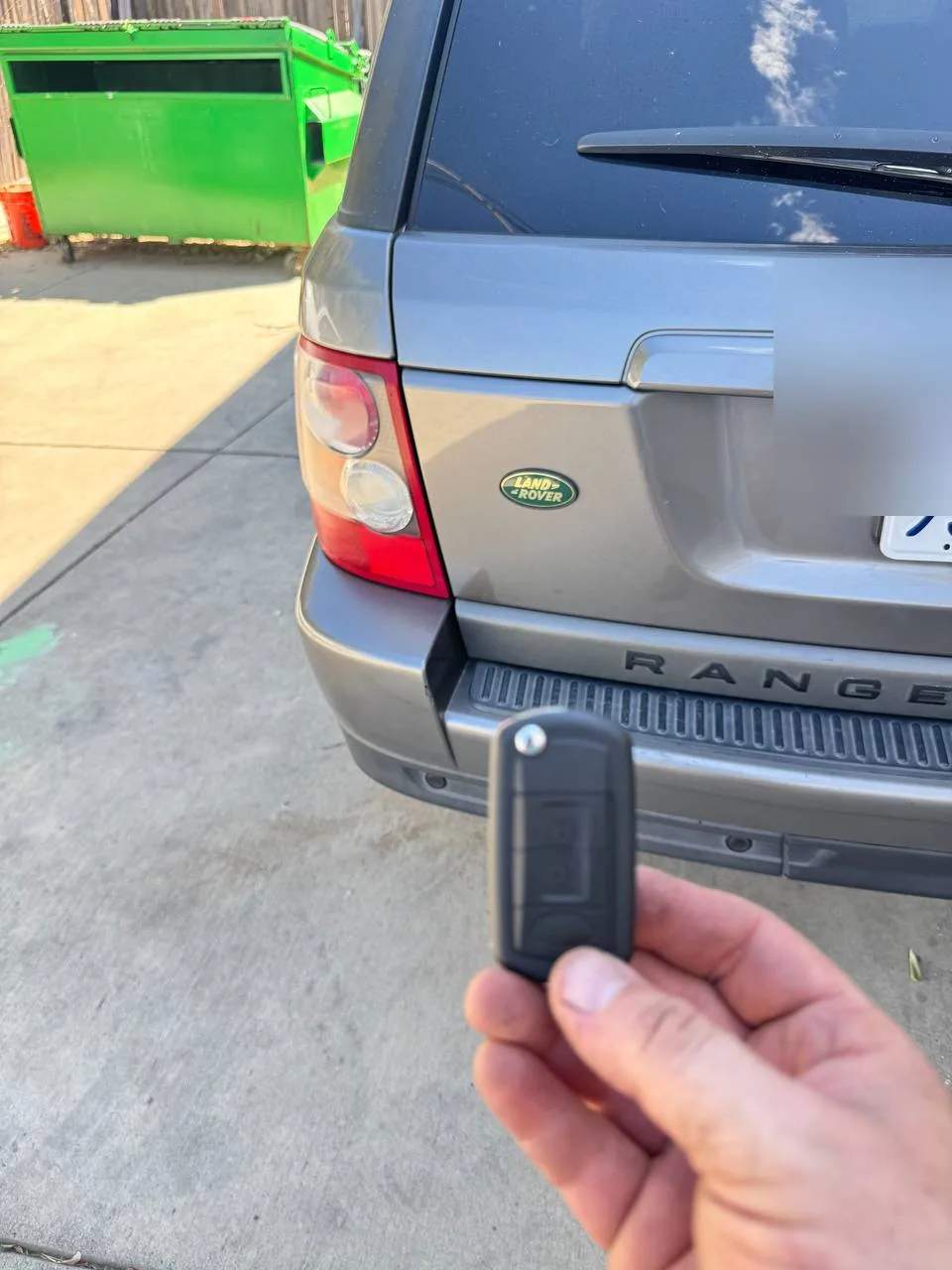 Locksmith holding a Range Rover key fob behind the vehicle during a locksmith service call