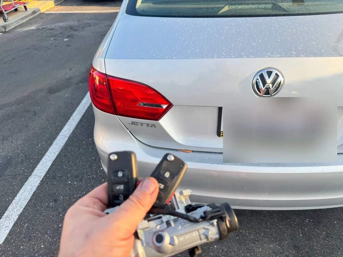 Locksmith holding a Volkswagen ignition lock cylinder and key fobs behind the vehicle