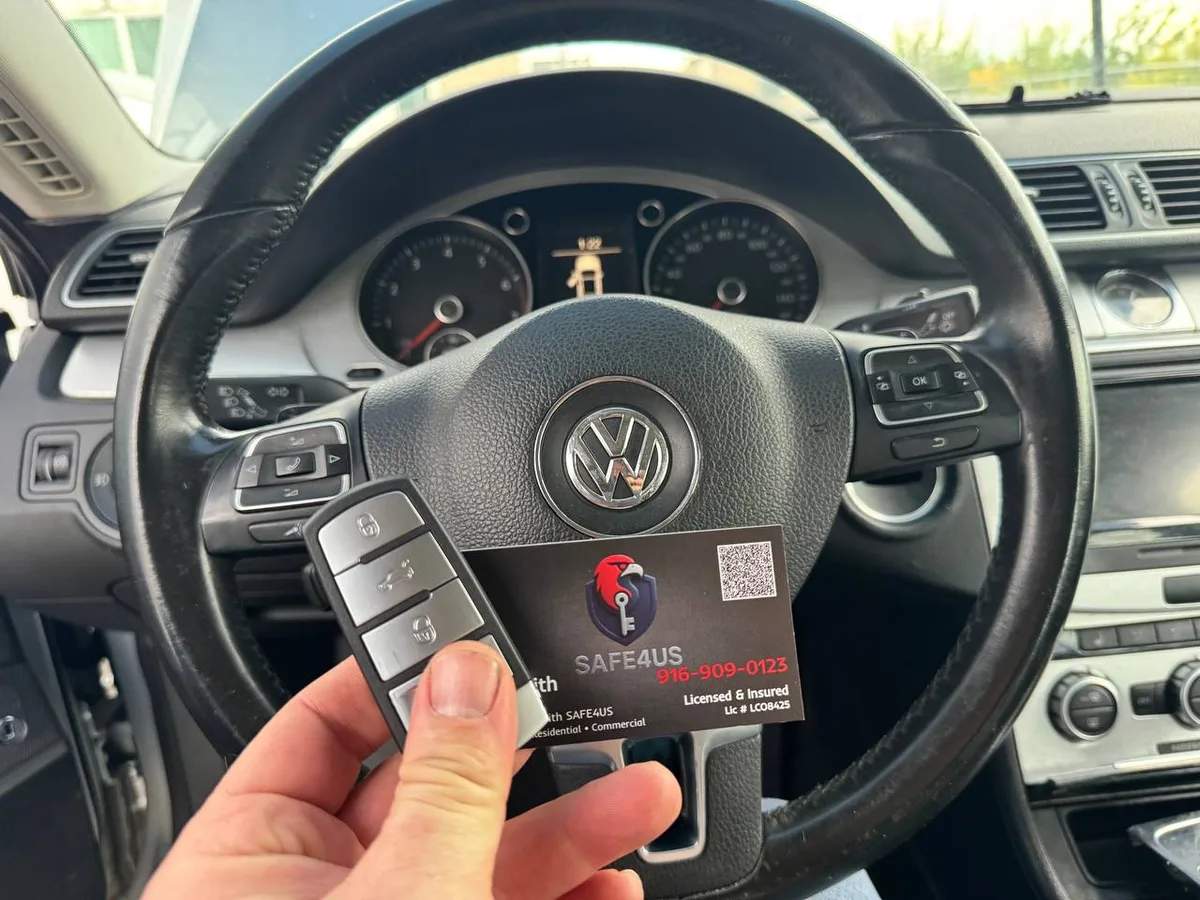 Locksmith holding a Volkswagen key fob and Safe4us business card beside the vehicle