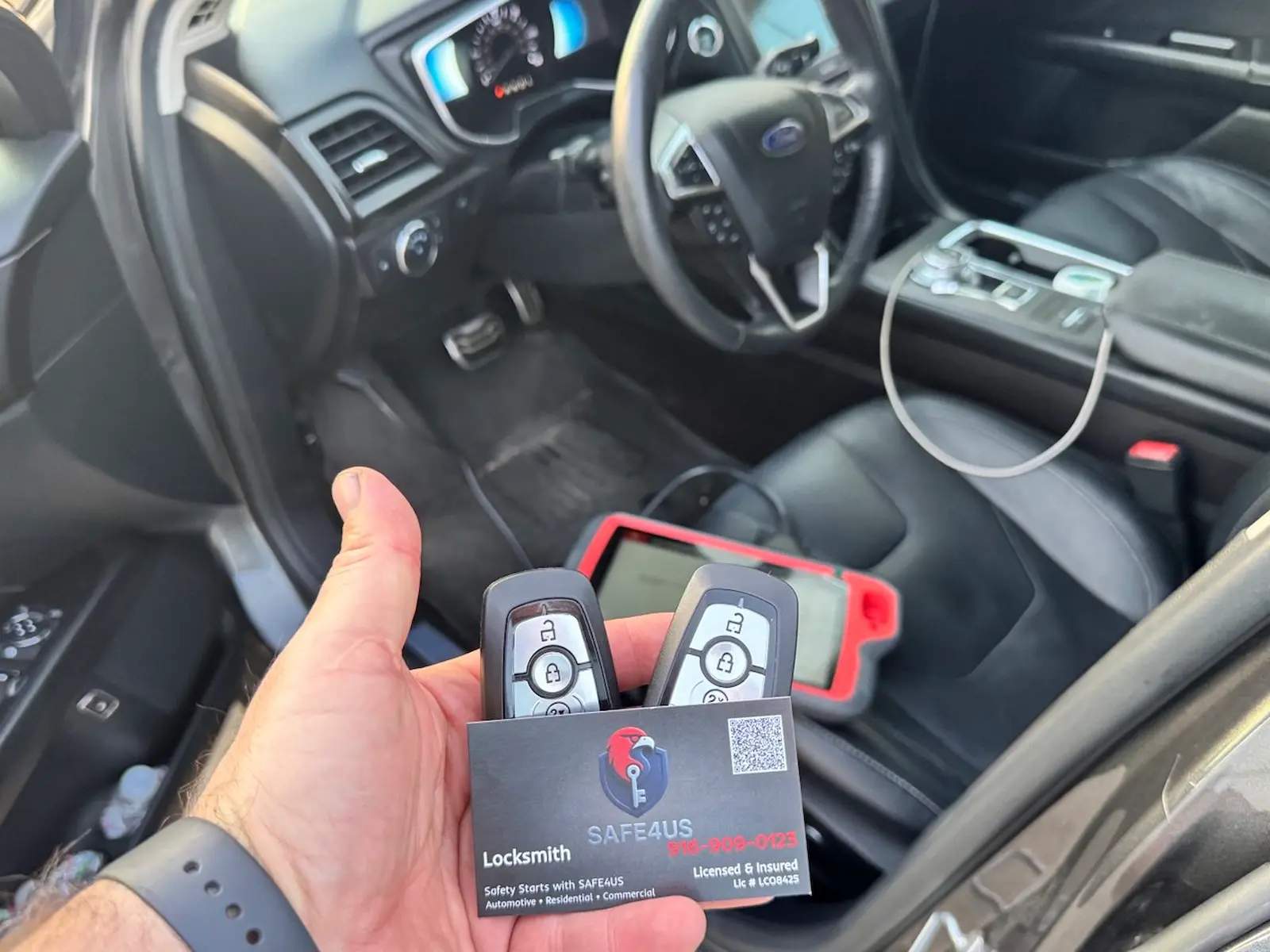 Hand holding two Ford proximity keys and a Safe4us card beside a diagnostic tablet in a vehicle