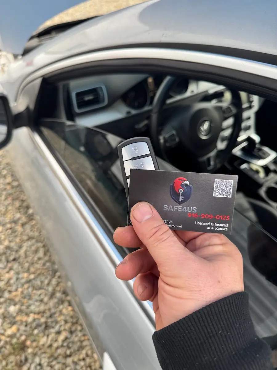Hand holding a key fob and Safe4us business card beside a silver vehicle with the hood raised