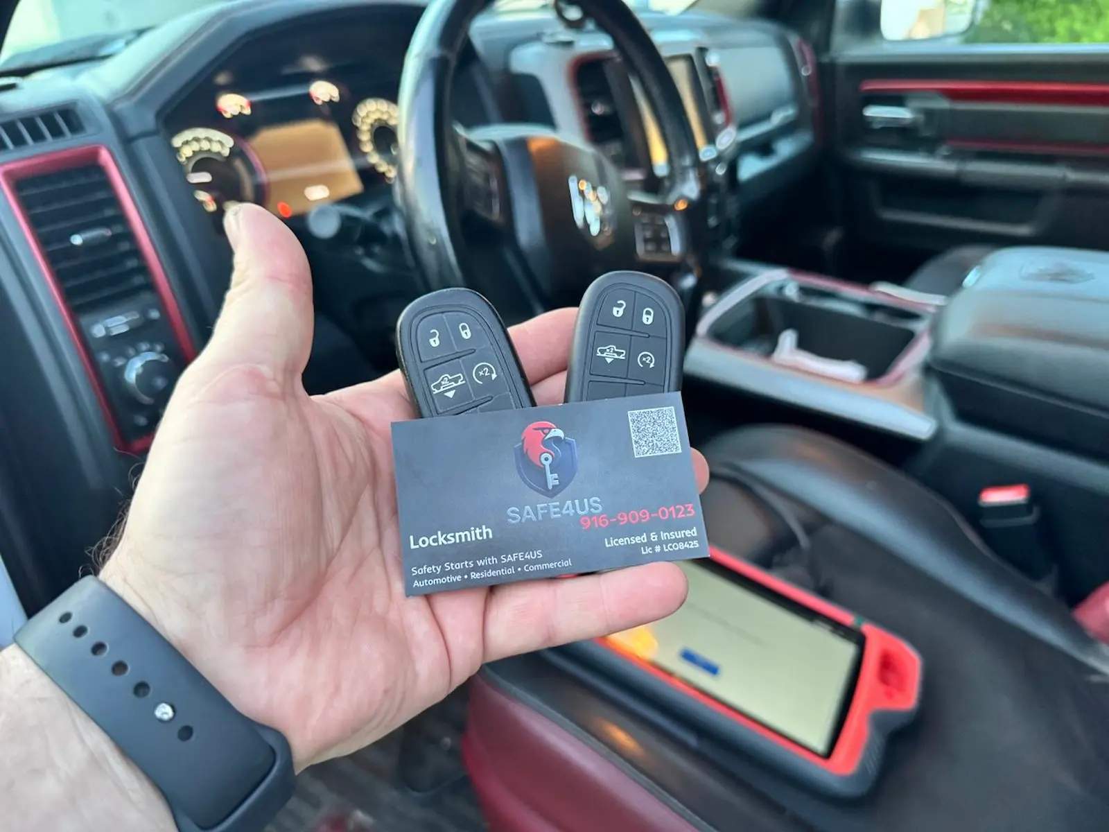 Hand holding two truck key fobs and a Safe4us card inside a Ram truck with a diagnostic tablet on the seat